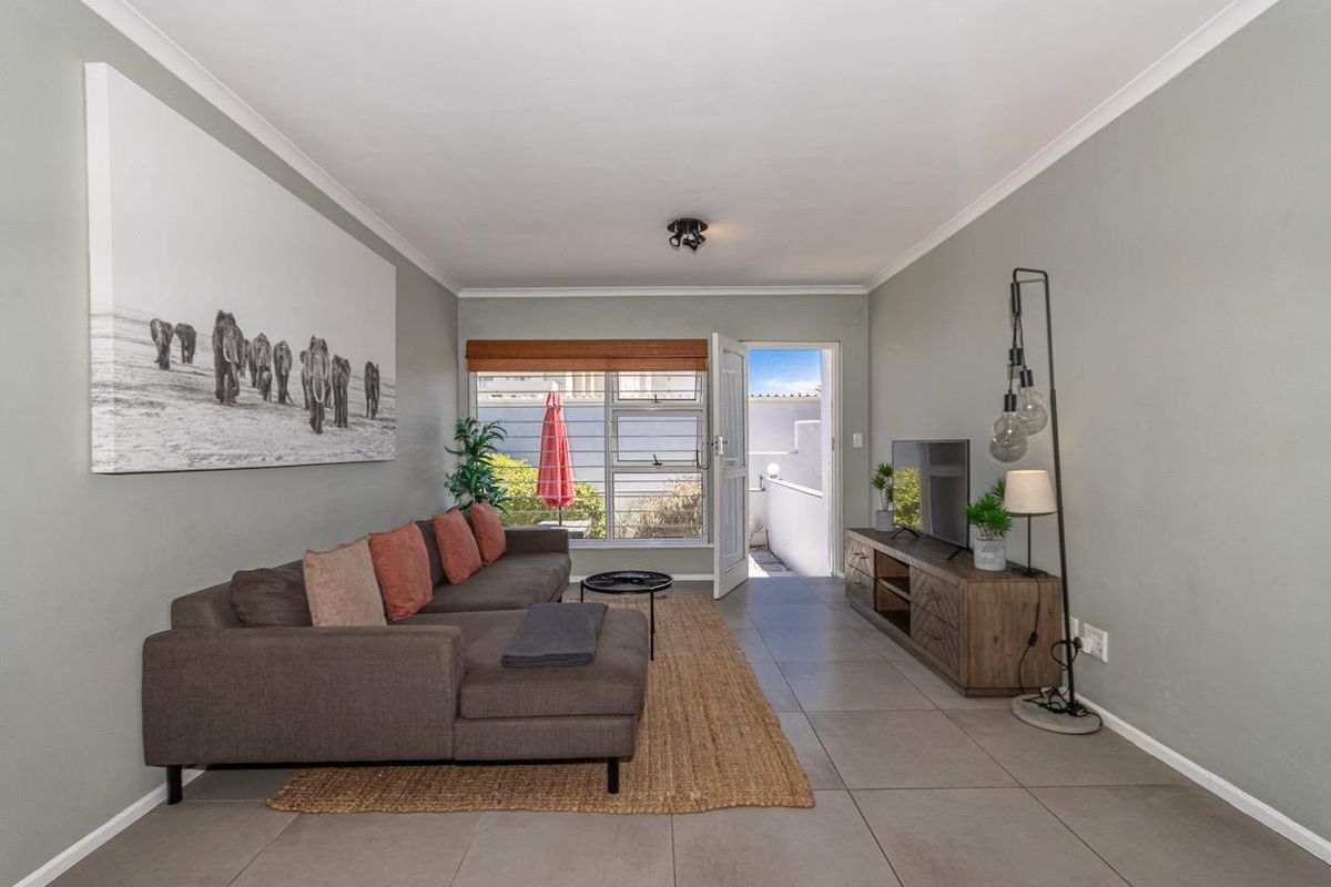A well-maintained living room featuring neutral tiled flooring, cove cornicing, and direct access to an outdoor area through an external door.