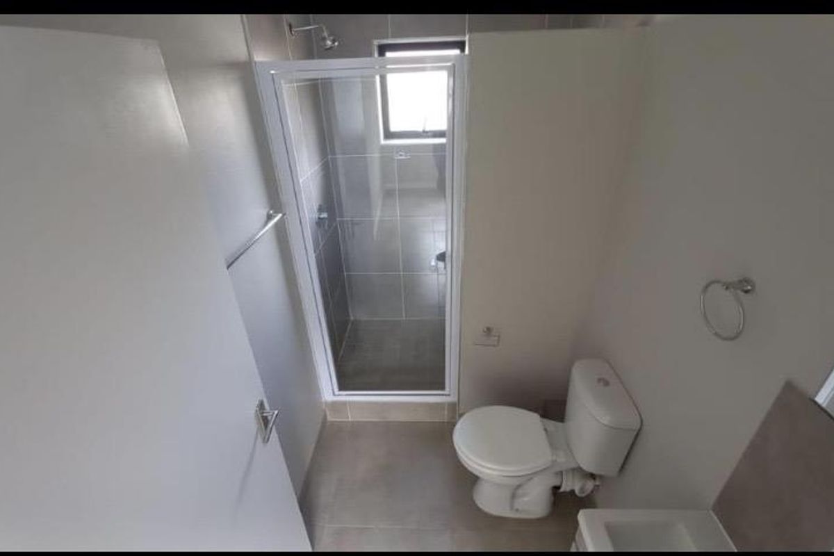 A clean, modern bathroom featuring a glass-enclosed shower, white toilet, and neutral floor tiling, presenting a functional and well-maintained space.
