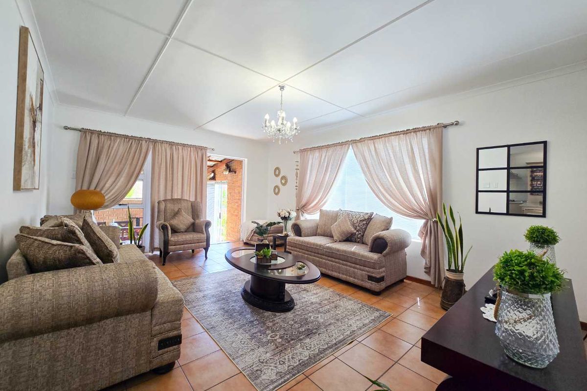 A spacious living room featuring tiled flooring, a classic chandelier, and large windows with curtains, providing access to an outdoor patio area.