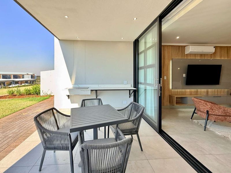 Modern covered patio featuring a built-in braai, tiled flooring, and seamless access to the living area through large sliding glass doors.
