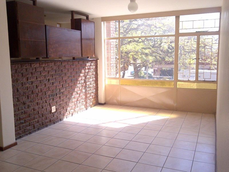 An empty living area featuring exposed brickwork, tiled flooring, and large windows providing natural light and street views.