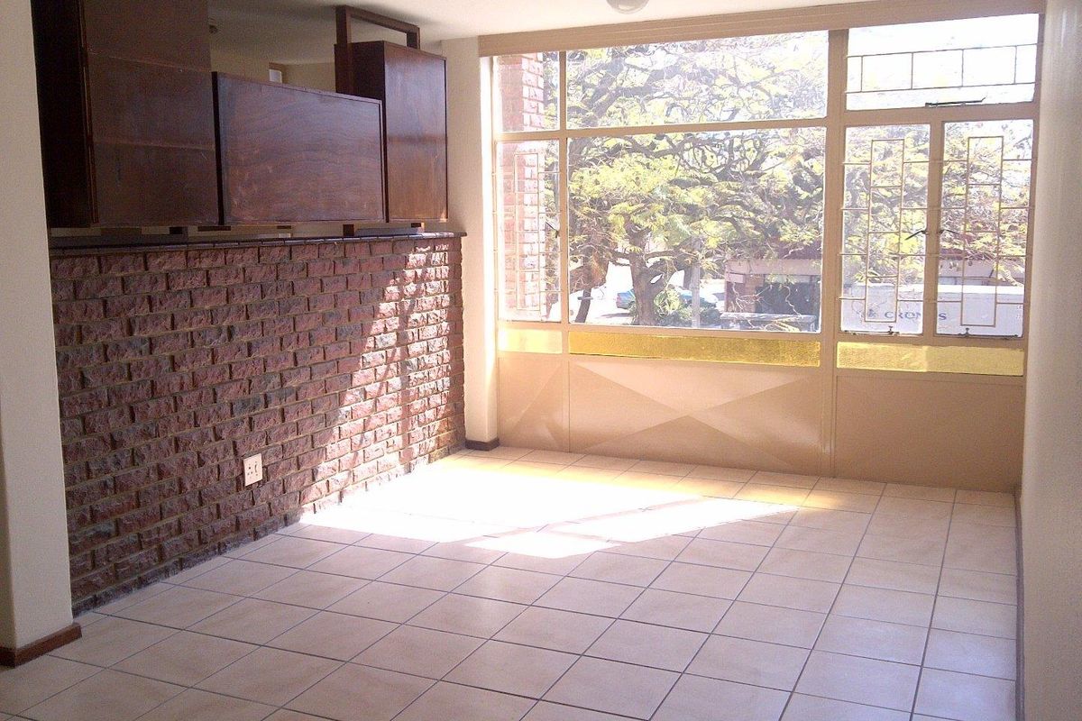 An empty living area featuring exposed brickwork, tiled flooring, and large windows providing natural light and street views.