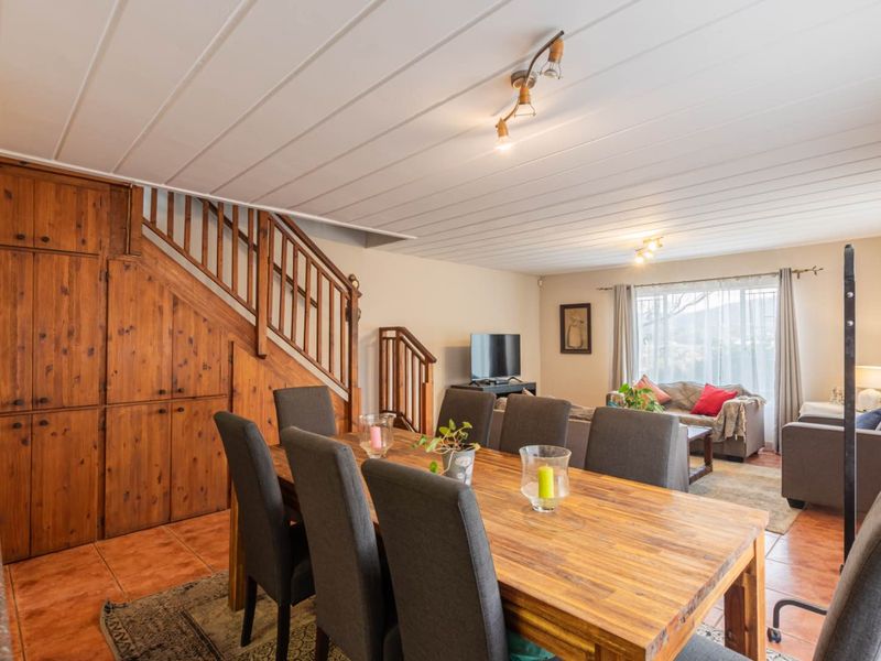 Open-plan living and dining area featuring tiled flooring, a timber staircase with integrated storage, and a tongue and groove ceiling.