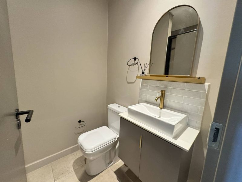 Modern guest bathroom featuring a sleek vanity with vessel sink, brass fixtures, subway tile backsplash, and an elegant arched mirror.