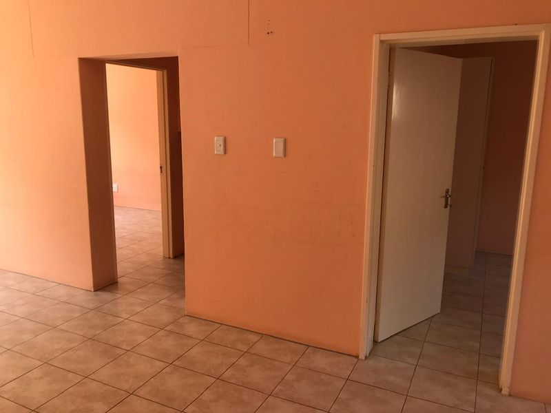 An empty hallway featuring ceramic floor tiles and access to adjacent rooms, requiring cosmetic updates to the wall finishes.