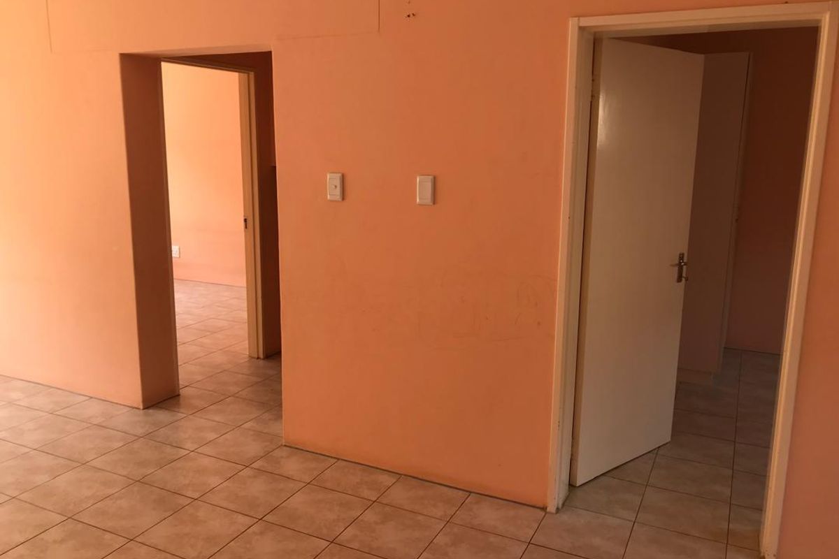 An empty hallway featuring ceramic floor tiles and access to adjacent rooms, requiring cosmetic updates to the wall finishes.