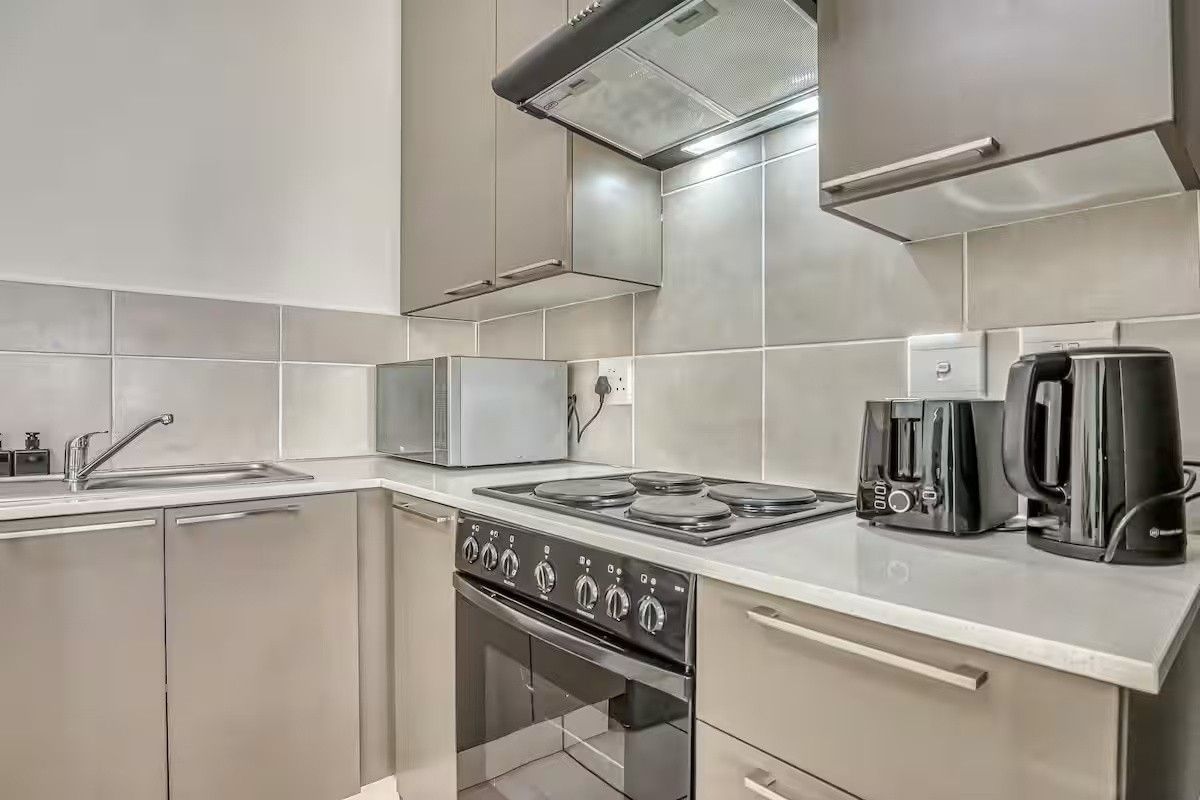 A modern, compact kitchen featuring sleek grey cabinetry, a built-in oven with electric hob, extractor fan, and a clean tiled backsplash.