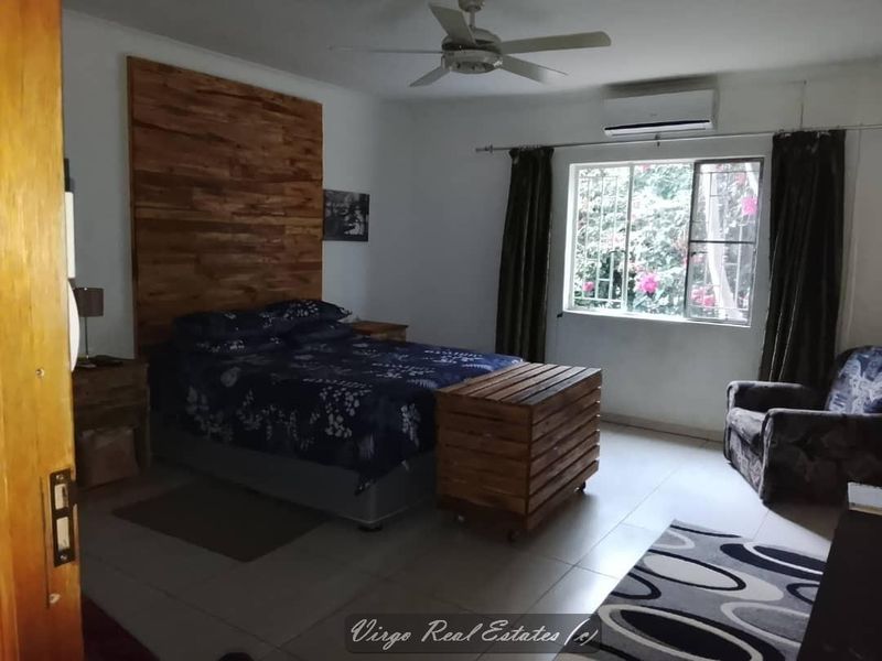Spacious bedroom featuring a timber accent wall, tiled flooring, ceiling fan, and a split-system air conditioner for climate control.