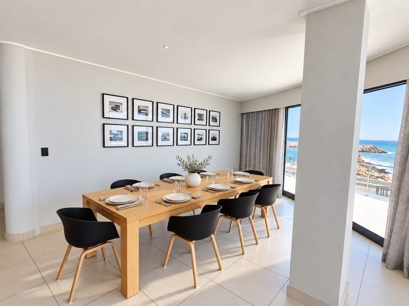 A bright and modern dining room featuring large format floor tiles, recessed lighting, and expansive sliding glass doors offering direct ocean views.