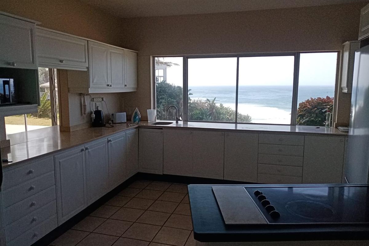 A functional kitchen featuring white cabinetry, tiled flooring, and a large window offering expansive ocean views.
