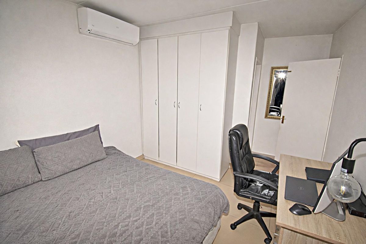 A functional bedroom featuring built-in wardrobes, tiled flooring, and a wall-mounted air conditioning unit.