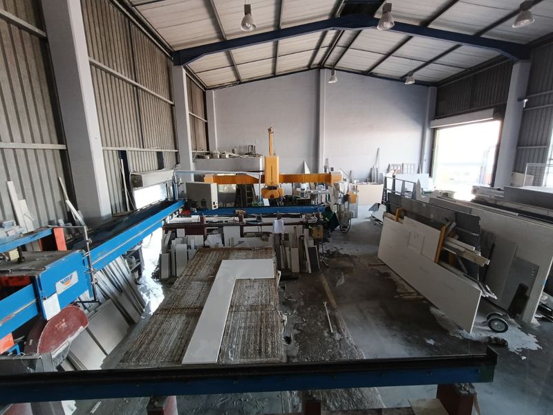 Industrial warehouse space featuring a large bridge saw, high-bay lighting, and durable concrete flooring, suitable for manufacturing or stone processing operations.