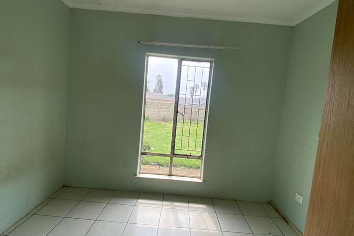 An empty bedroom featuring tiled flooring, a window with security bars, and a built-in cupboard, offering a blank canvas for renovation.