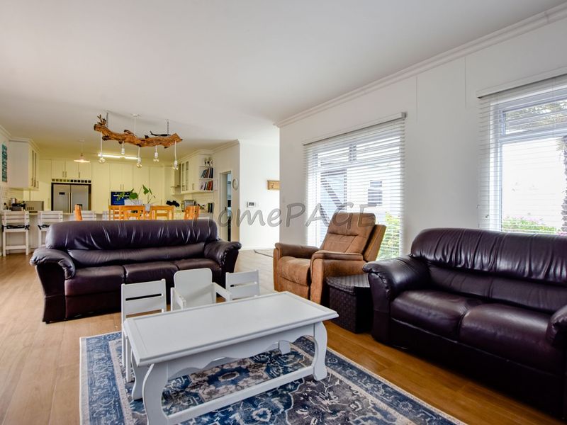 Spacious open-plan living area featuring laminate flooring, coved cornicing, and a seamless flow into a well-appointed kitchen with ample cabinetry.