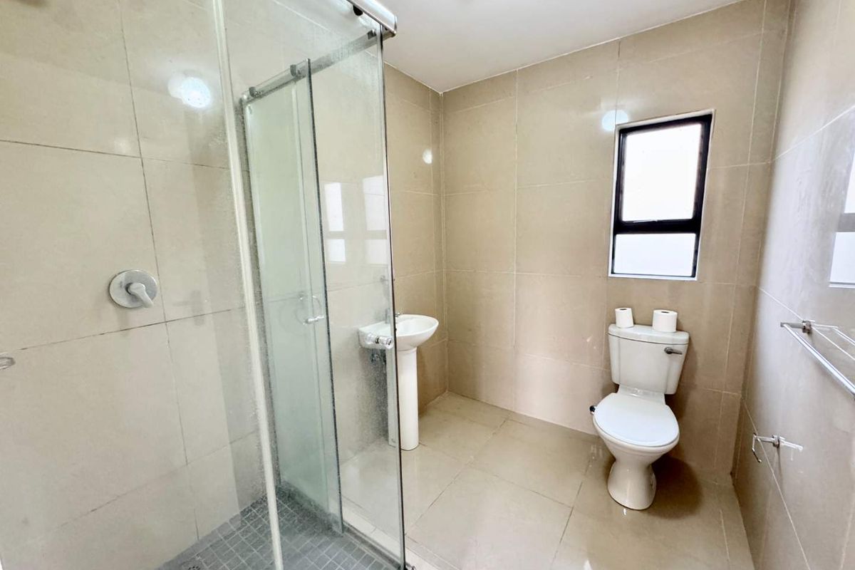A clean, modern bathroom featuring a glass-enclosed shower, pedestal basin, and toilet with neutral floor-to-ceiling tiling.