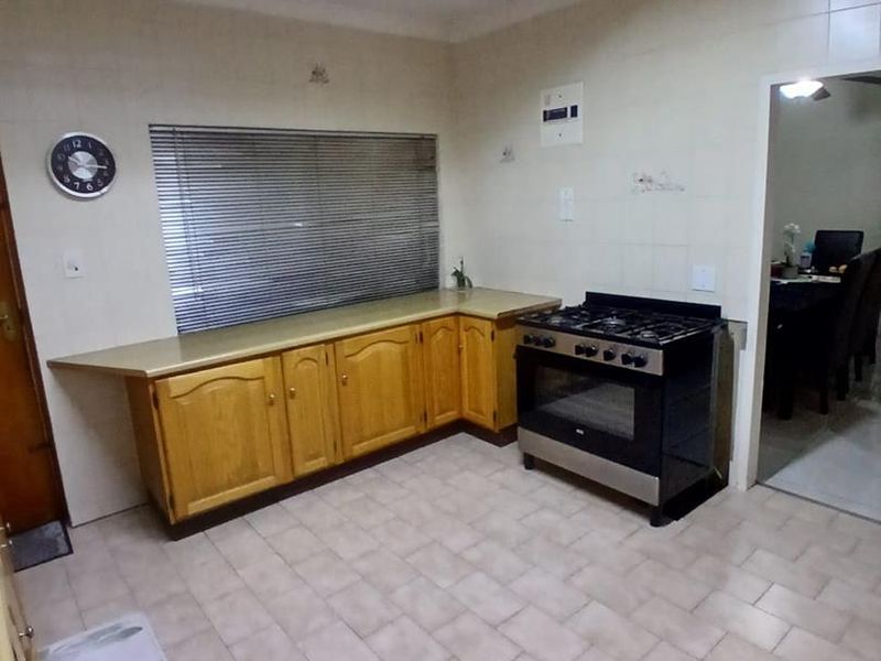 A functional kitchen featuring wooden cabinetry, a gas stove, tiled flooring, and a tiled splashback, offering a practical layout for daily cooking.