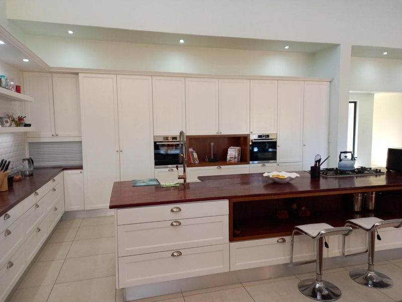 Modern kitchen featuring white cabinetry, dark wood countertops, a large central island with breakfast bar seating, and integrated stainless steel appliances.