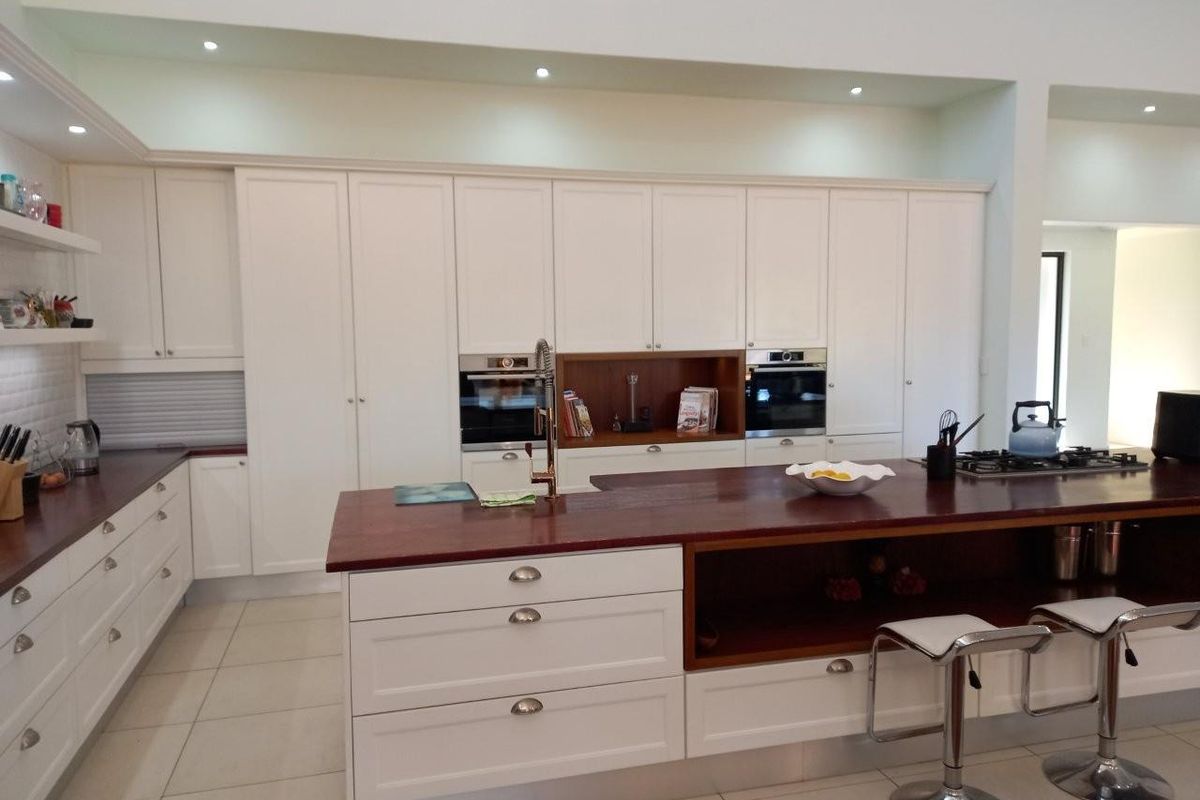 Modern kitchen featuring white cabinetry, dark wood countertops, a large central island with breakfast bar seating, and integrated stainless steel appliances.