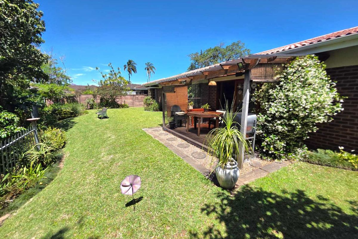 A well-maintained rear garden featuring a covered timber pergola patio, brick exterior walls, and a spacious lawn area.