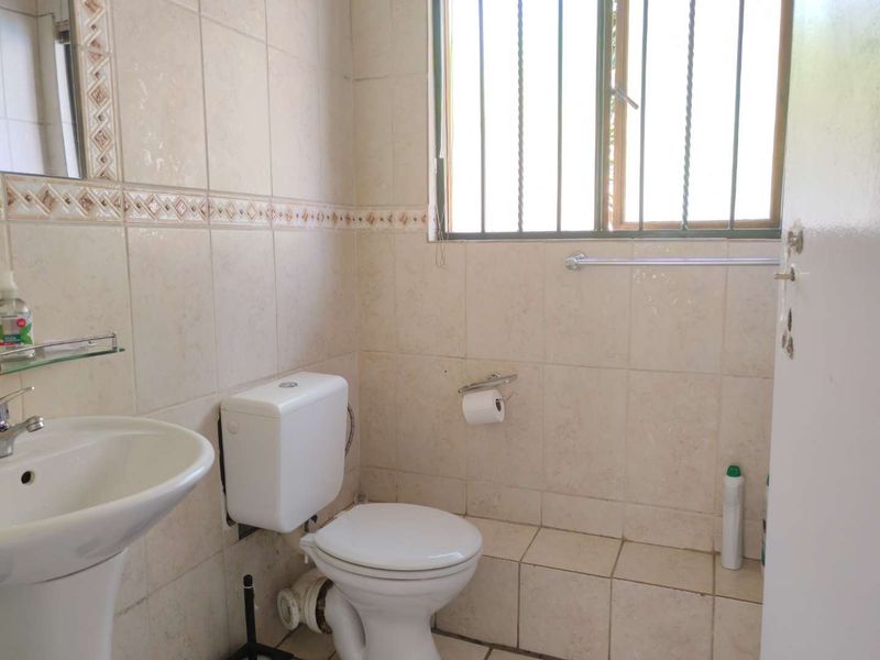 A functional bathroom featuring tiled walls and flooring, a pedestal basin, and a toilet with security bars on the window.