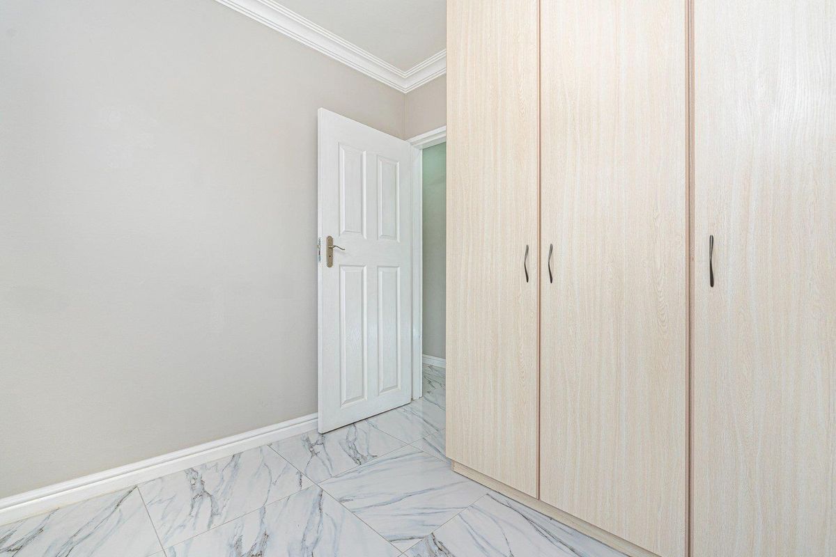 A bright bedroom featuring light wood-grain built-in cupboards, modern marble-look floor tiles, and crisp white crown molding.