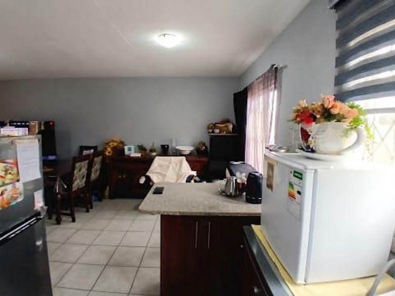 Open-plan living and kitchen area featuring tiled flooring, a central kitchen island, and neutral wall tones, offering a functional and versatile living space.