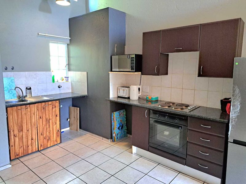 Kitchen featuring dark cabinetry, granite countertops, built-in oven, electric hob, and tiled flooring with a functional layout.
