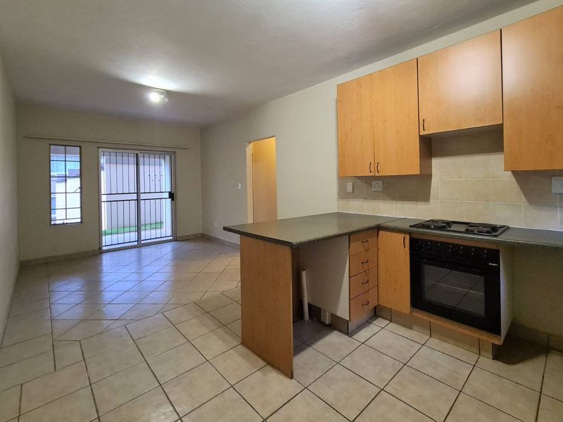 Open-plan kitchen and living area featuring tiled flooring, built-in cabinetry with integrated oven and hob, and sliding door access to the exterior.