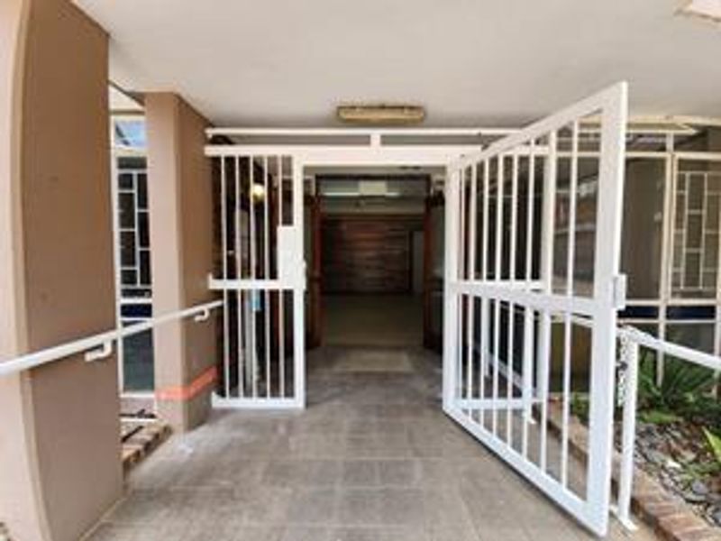 Entrance area featuring a white security gate, tiled flooring, and a handrail leading into the building interior.