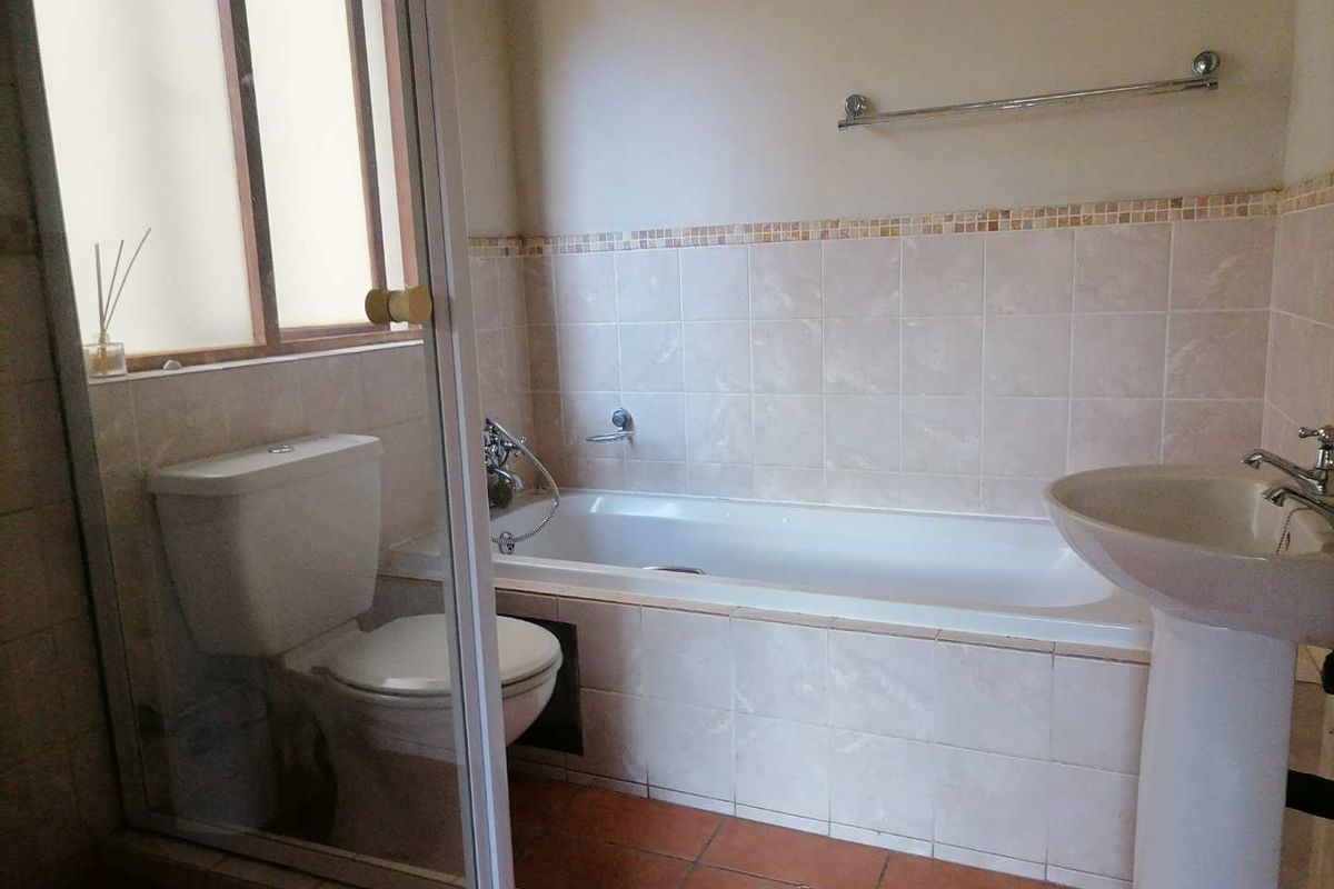 A functional bathroom featuring a built-in bathtub, pedestal sink, and toilet, finished with neutral wall tiles and terracotta-style floor tiles.