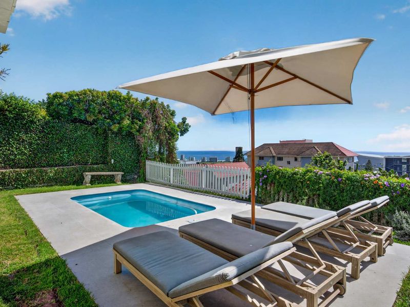 Outdoor pool area featuring a paved deck, swimming pool, and landscaped garden with ocean views.