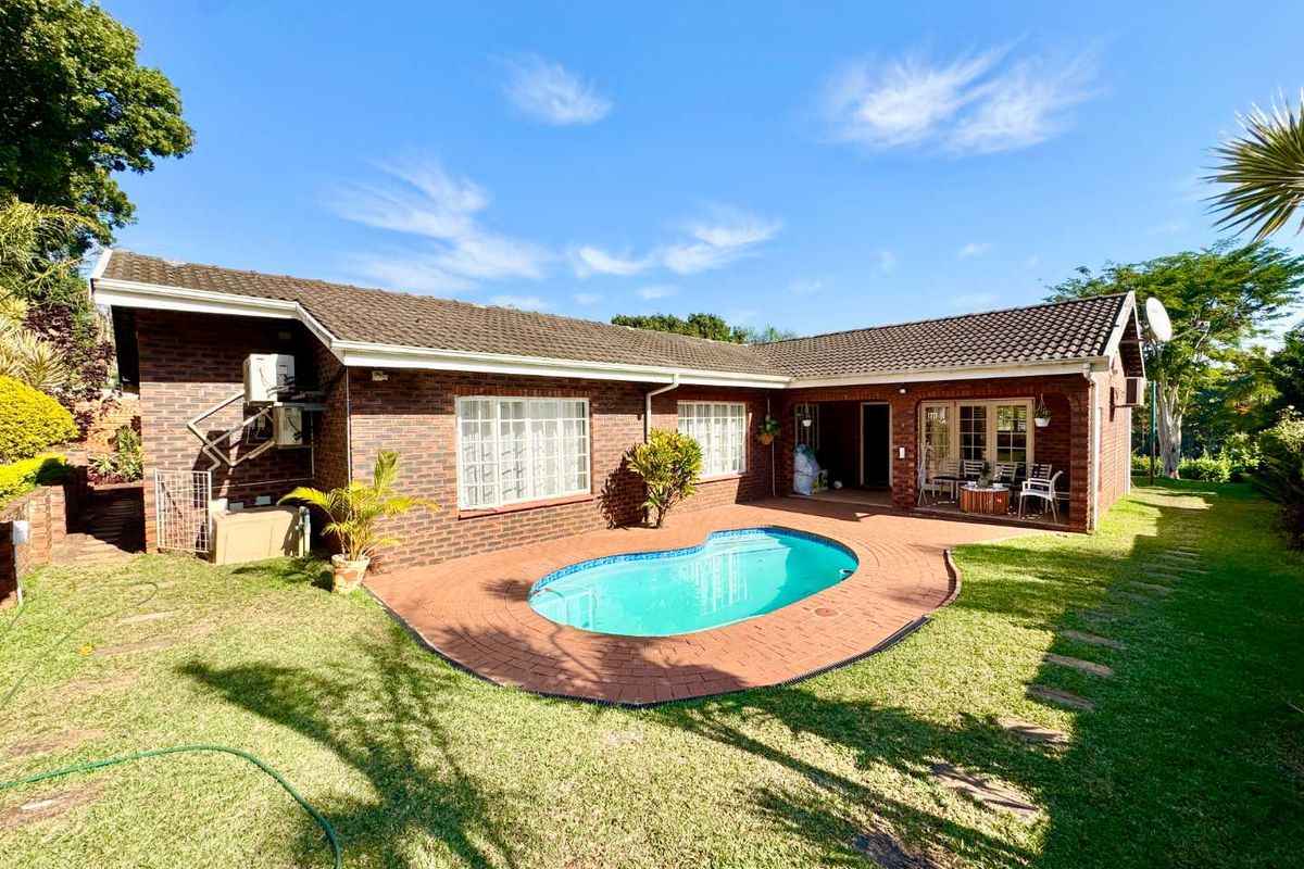 Rear view of a face brick house featuring a swimming pool, paved patio area, and well-maintained garden surroundings.