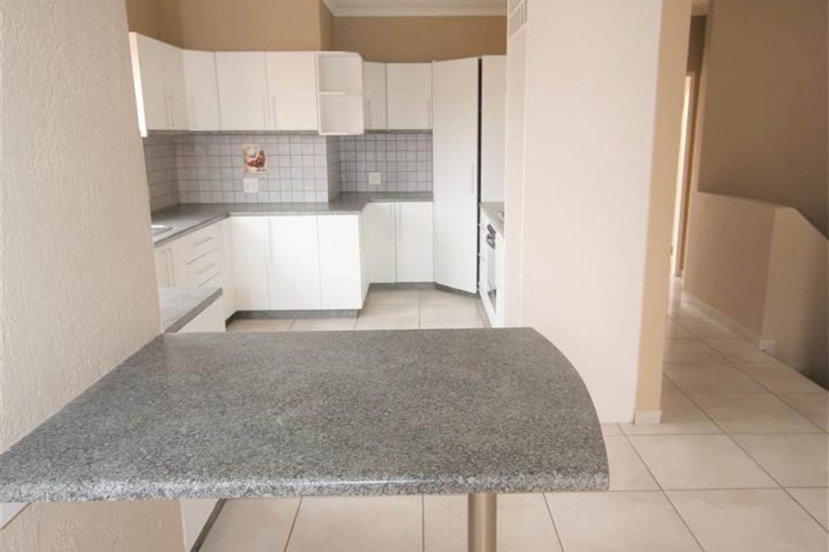 A functional kitchen featuring white cabinetry, tiled splashbacks, and a breakfast bar with a stone-look countertop, set against neutral tiled flooring.
