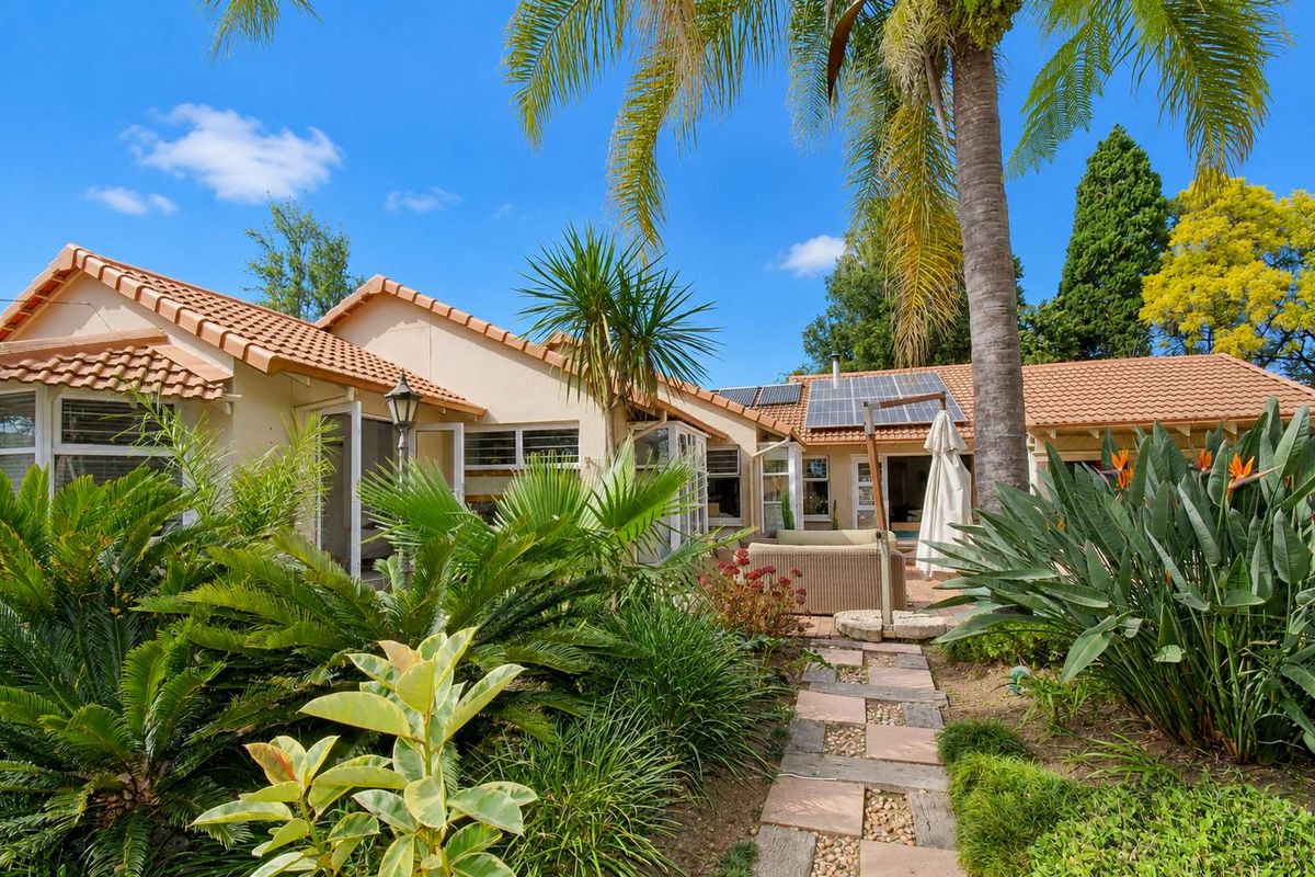 A well-maintained rear exterior view of the house featuring a terracotta tiled roof, solar panels, and a landscaped garden with a paved walkway.