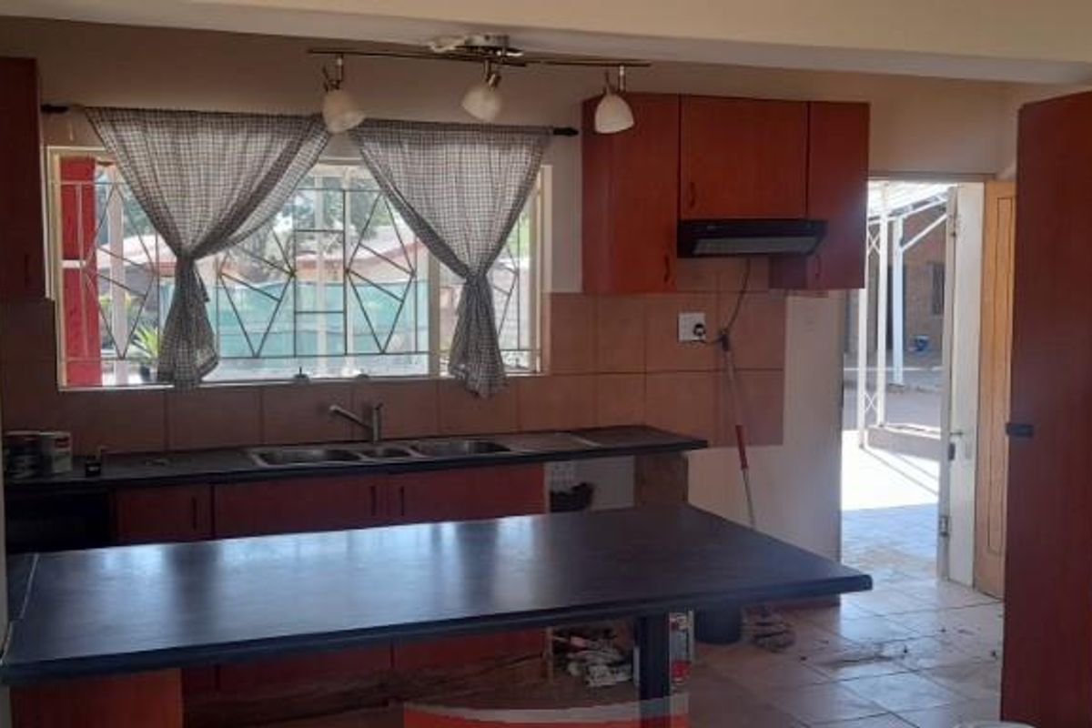 A functional kitchen featuring wooden cabinetry, a breakfast bar, double sink, and an integrated extractor fan, with direct access to the rear exterior.