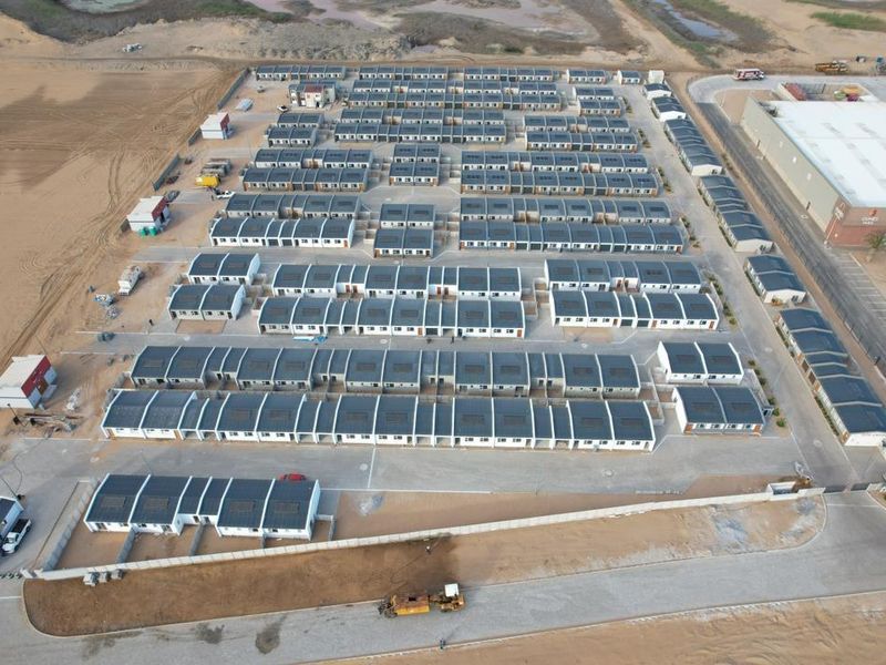 Aerial view of a modern townhouse development featuring uniform residential units, paved access roads, and perimeter security fencing.