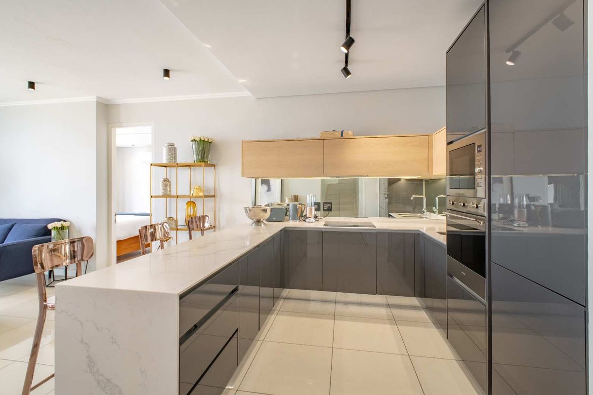 Modern open-plan kitchen featuring high-gloss cabinetry, stone countertops, integrated oven, and sleek track lighting in a contemporary penthouse setting.