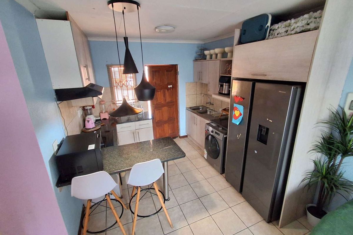 Compact kitchen featuring built-in cabinetry, a breakfast bar, integrated sink, and space for appliances, with direct access to an exterior door.