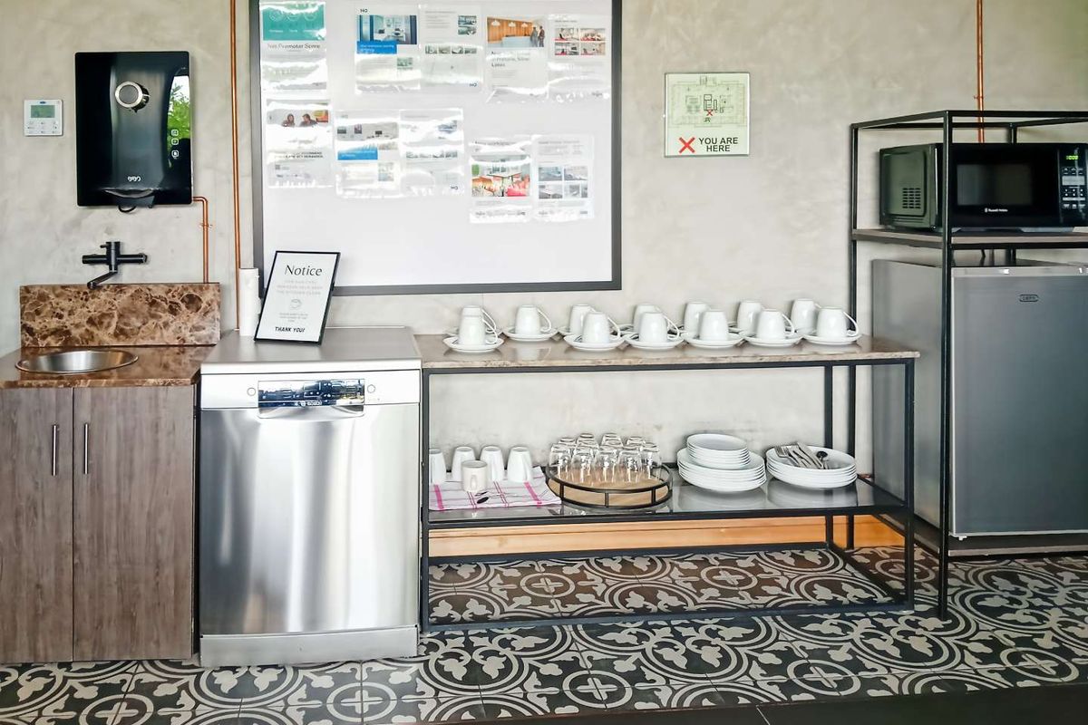 A functional office kitchenette area featuring a built-in sink, dishwasher, and open shelving for beverage service and storage.