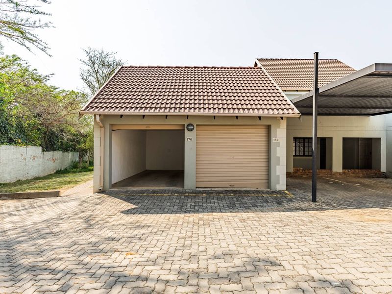 A double garage featuring one open bay and one roller shutter door, complemented by an adjacent carport and paved driveway area.