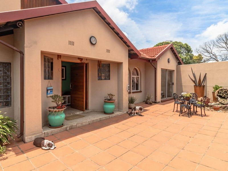 A spacious rear patio area featuring terracotta tiling, glass block accents, and access to the home through a main entrance and sliding glass doors.