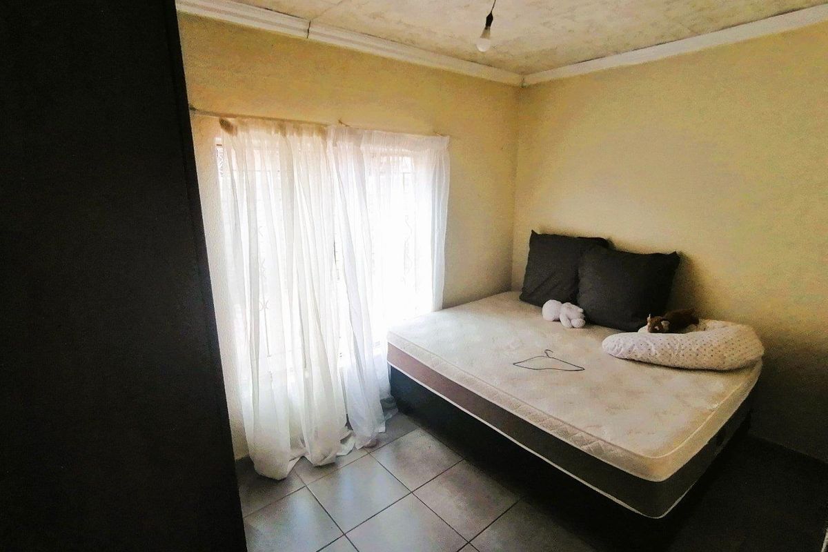 A compact bedroom featuring tiled flooring and a window with security bars, offering a functional space ready for cosmetic updates.