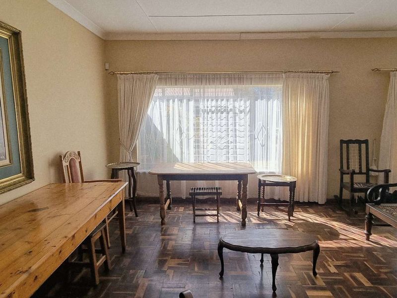 Spacious living room featuring classic parquet flooring and large windows with security bars, offering a bright and traditional living space.