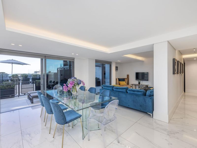 Modern open-plan living and dining area featuring high-quality marble-look flooring, recessed cove lighting, and large sliding glass doors leading to a private balcony.