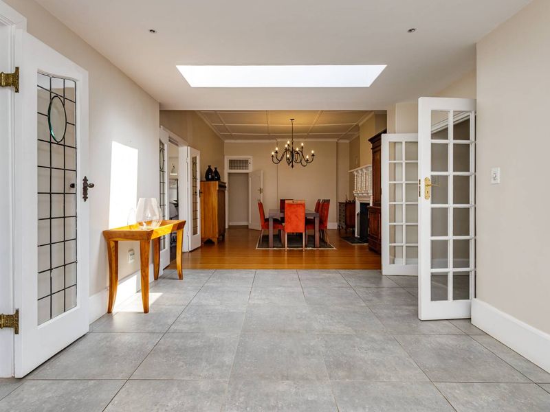 Spacious open-plan living area featuring a large skylight, a blend of tiled and hardwood flooring, and elegant French doors connecting the spaces.