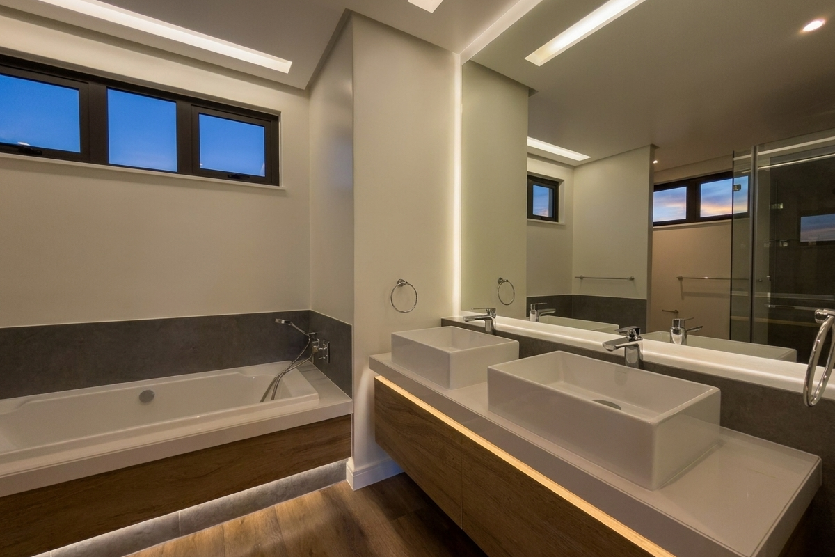Modern bathroom featuring a floating double vanity with vessel sinks, integrated LED lighting, a built-in bathtub, and a glass-enclosed shower.