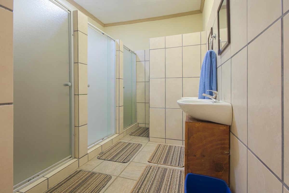 A functional communal bathroom facility featuring multiple shower cubicles with frosted glass doors and wall-mounted ceramic washbasins.