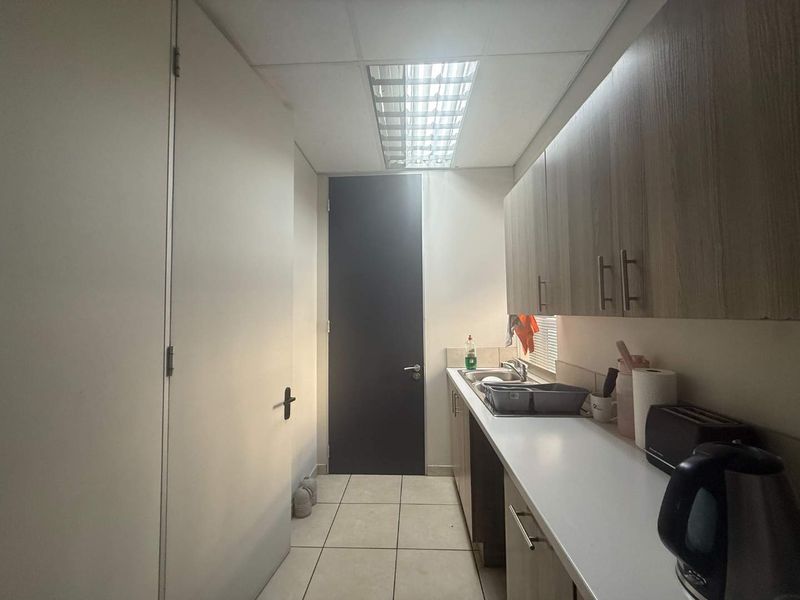 A functional office kitchenette featuring built-in cabinetry, a stainless steel sink, laminate countertops, and tiled flooring under a drop ceiling.