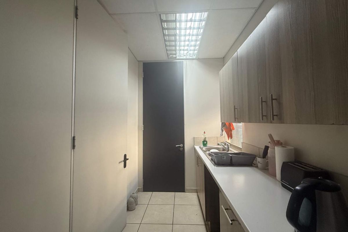 A functional office kitchenette featuring built-in cabinetry, a stainless steel sink, laminate countertops, and tiled flooring under a drop ceiling.