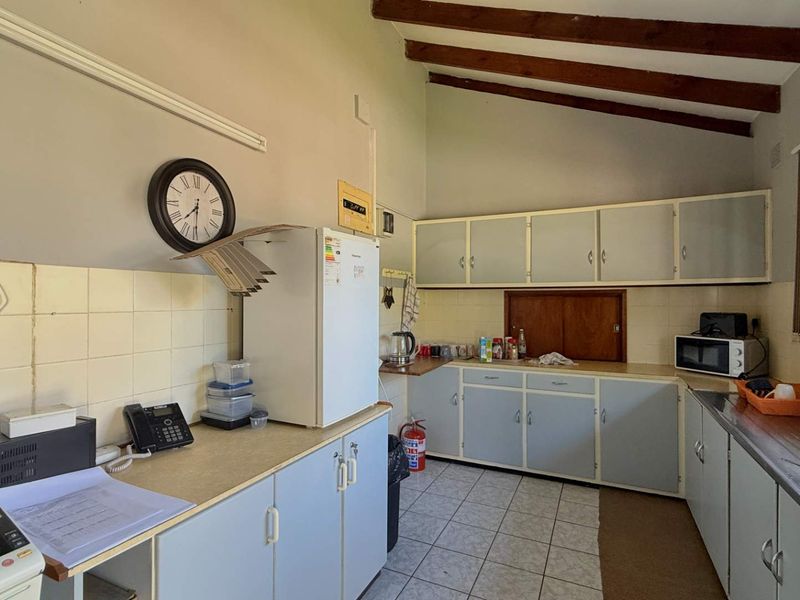 A functional kitchen featuring built-in cabinetry, laminate countertops, a stainless steel sink, and exposed timber ceiling beams, offering potential for modernization.